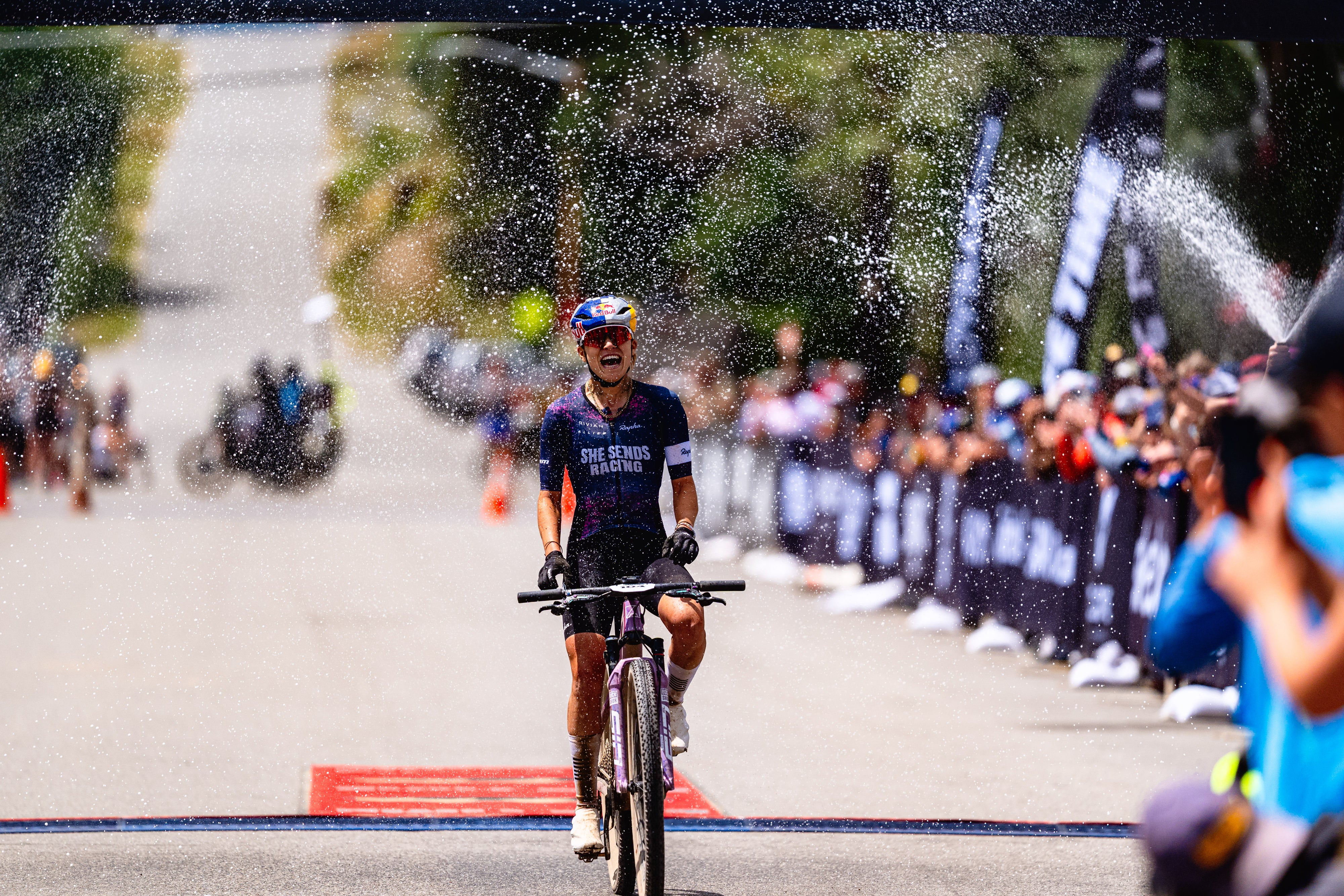 Kate Courtney crossing finish line with champagne 2025
