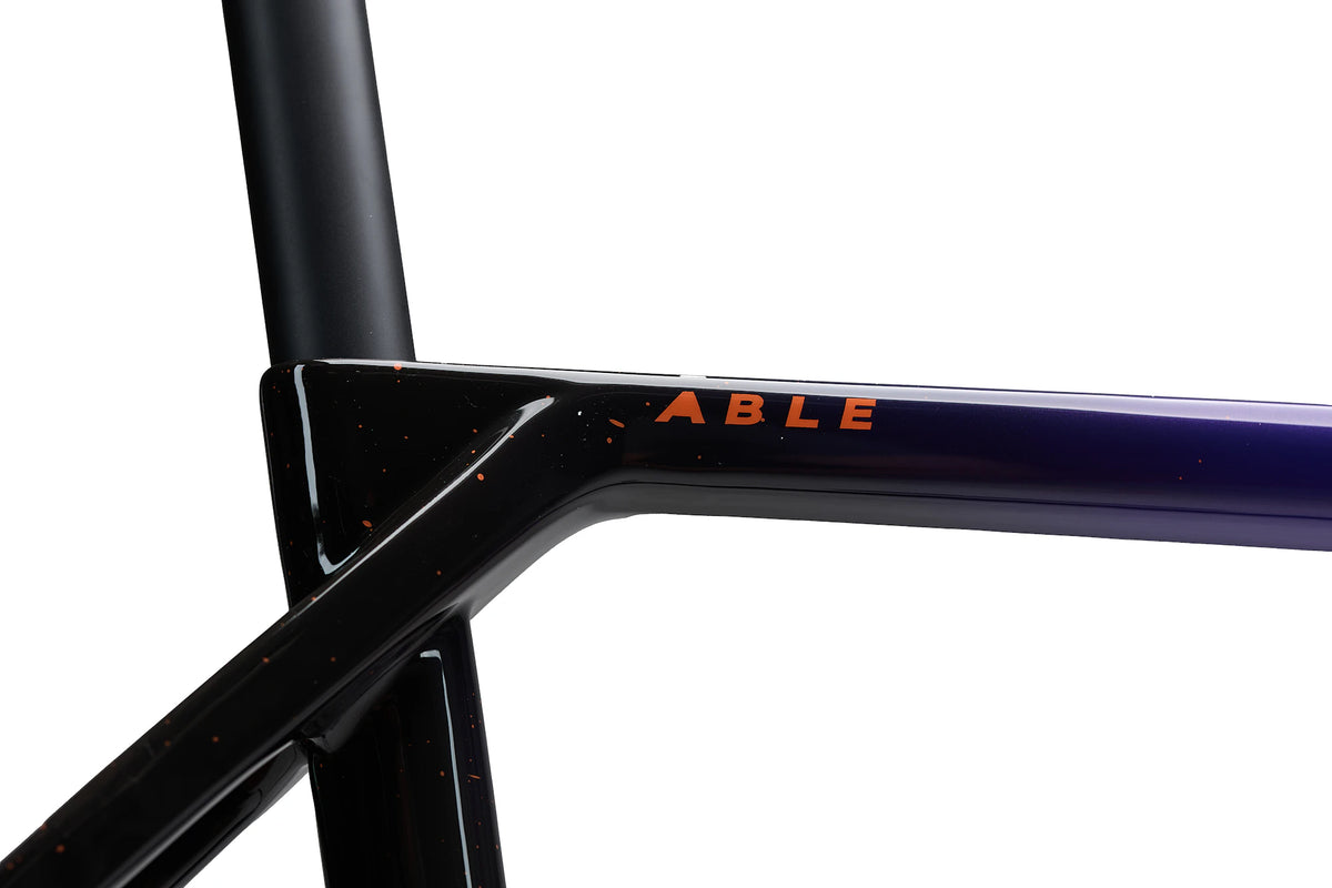 Close-up of the ABLE top tube decal in coral on the black section of the Last Light paint, with coral splatter
